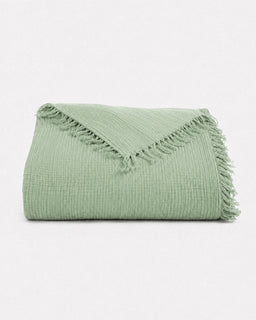 A folded sage green textured throw blanket with fringed edges, displayed on a clean white background.