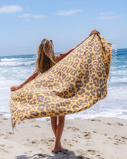 Person holding a leopard print towel on a beach with ocean view