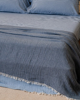 Blue textured blanket on a bed with striped pillows