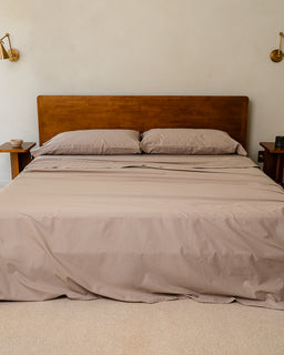 Bed with beige bedding and headboard in a room with beige walls and wooden nightstands.