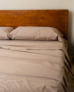 Beige bedding on a bed with a wooden headboard against a plain wall.