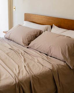 Neatly made bed with beige bedding and pillows in a bedroom setting.
