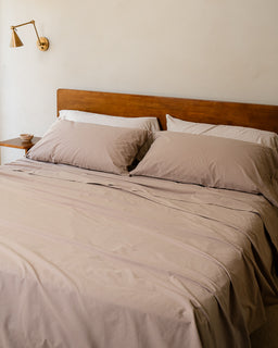 Bed with brown bedding and pillows in a room with a wall lamp.