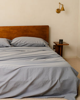 Bed with gray bedding and wooden headboard in a room with a wall sconce.