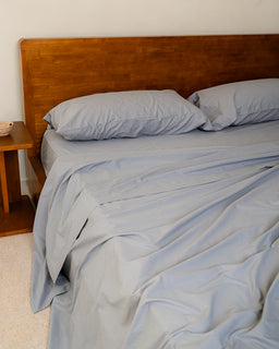 Bed with light blue bedding and pillows against a wooden headboard.