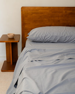Bed with wooden headboard and gray bedding next to a wooden side table.
