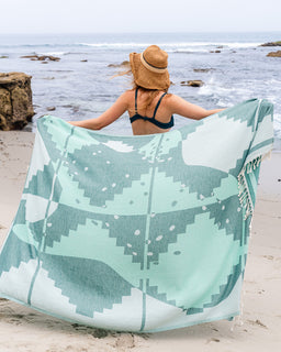 Woman on a beach with a large green and white patterned towel