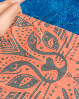 Close-up of a towel with a geometric pattern in gray on an orange background, held over blue water.
