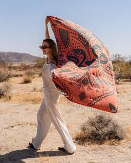 Woman holding a large orange and black patterned fabric in a desert setting