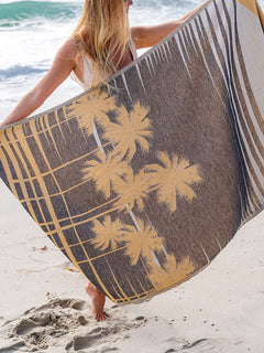Person holding a beach towel with palm tree design on a sandy beach.