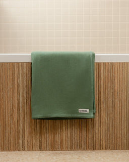 Green towel hanging on a wooden rack with a neutral wall background