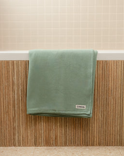 Green towel hanging on a wooden rack against a beige wall.