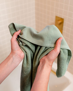 Person holding a green towel in front of a bathroom mirror.
