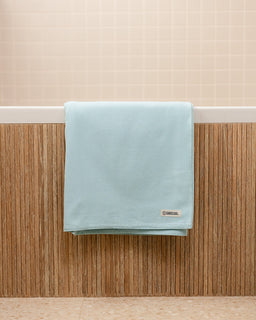 Light blue towel hanging on a wooden rack against a beige wall