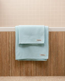 Light blue towel hanging on a wooden rack against a beige wall