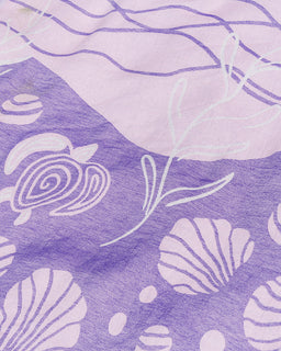 A close-up of a purple and light lavender patterned fabric with white seashell and abstract line illustrations.