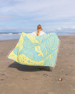 Person holding a large yellow and blue patterned towel on a beach