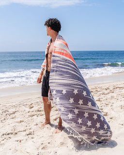 Person on a beach with a star-patterned towel draped over their shoulders