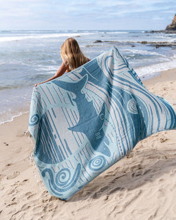 Person sitting on a beach with a blue and white patterned towel featuring starfish designs.