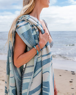 Woman on a beach holding a striped towel with ocean and sky in the background