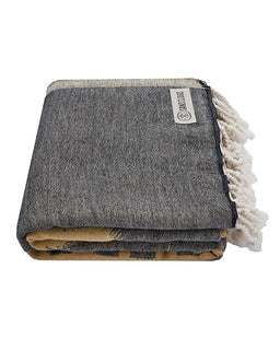 Folded blanket with tassels and a visible brand label on a white background