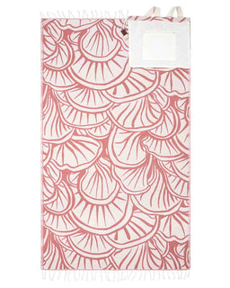 A rectangular textile product, likely a towel or blanket, featuring a repeating scallop shell pattern in dusty pink on a white background, with white fringed edges and a small white label near the top.