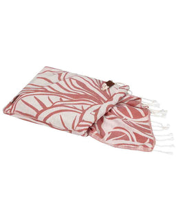 A folded cotton Turkish towel with a coral pink and white botanical leaf pattern, featuring white fringed edges and a small brown leather tag.