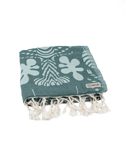 Teal towel with white floral patterns and tassels on a white background