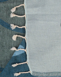 Close-up of a textured fabric with blue and gray gradient and white tassels.