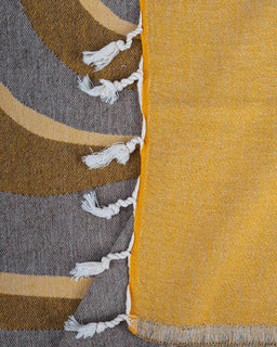 Close-up of a textured fabric with geometric patterns and tassels on a yellow and gray background.