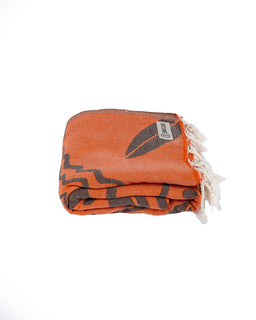 Folded orange towel with black patterns and white fringe on a white background