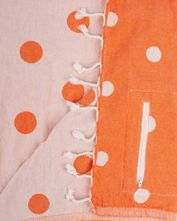 Close-up of fabric with orange polka dots and a zipper on a pink background