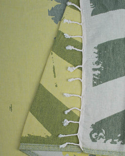 Green and white patterned towel with tassels on a yellow background