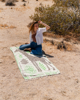 Woman sitting on a patterned towel in a desert setting