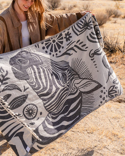 Person holding a large towel with zebra design in a desert setting