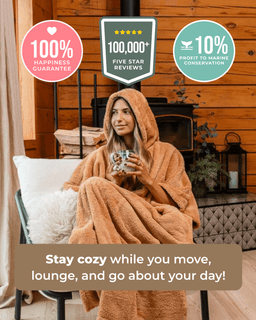 A woman wrapped in a plush tan hooded blanket sits in a cozy room with wood-paneled walls, holding a mug. Promotional text and badge graphics appear around the photo, including 'Stay cozy while you move, lounge, and go about your day!' and trust badges for happiness guarantee and five-star reviews.