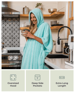 A woman in a kitchen wrapped in a light aqua hooded towel robe, holding a mug. Three feature icons at the bottom read Oversized Hood, Deep Side Pockets, and Extra Long Length.