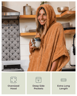 A woman in a kitchen wearing a plush hooded towel wrap or poncho in a warm tan/caramel color, holding a mug. Three feature callouts at the bottom read: Oversized Hood, Deep Side Pockets, and Extra Long Length.